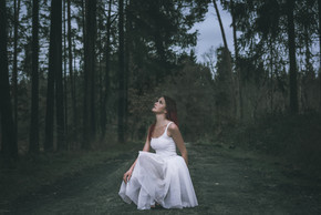 美麗的女人，發型，穿著白色芭蕾舞短裙，蹲著，在森林路上，抬頭，在春天的林地里。