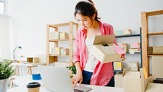 年輕的亞洲企業家女商人檢查庫存的產品采購訂單，并保存到家庭辦公室的電腦筆記本電腦工作。小企業主、在線市場交付、生活方式自由職業者概念。