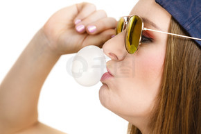 女人休閑風格的少女帽頭戴太陽鏡，用口香糖特寫做泡泡。青春風采。用口香糖做泡泡的女人