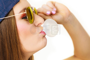 女人休閑風格的少女帽頭戴太陽鏡，用口香糖特寫做泡泡。青春風采。用口香糖做泡泡的女人