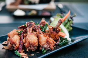 泰式炸雞翅、雞鼓配香草、辣椒、大蒜和蔬菜在黑盤上