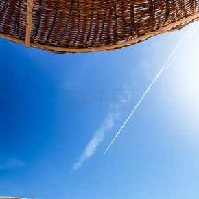 美麗的照片防曬稻草傘在沙灘上反對藍天和飛行的飛機。在海邊的稻草陽傘。暑假或假期的完美形象。復制空間.. 沙灘上的防曬稻草傘與藍天和飛行飛機的美麗形象。在海邊的稻草陽傘。暑假或假期的完美形象。您的文本的