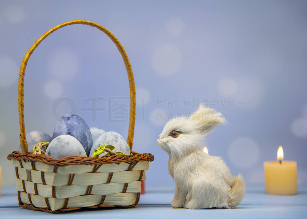 A bunny next to a basket full of Easter eggs on a wooden table o