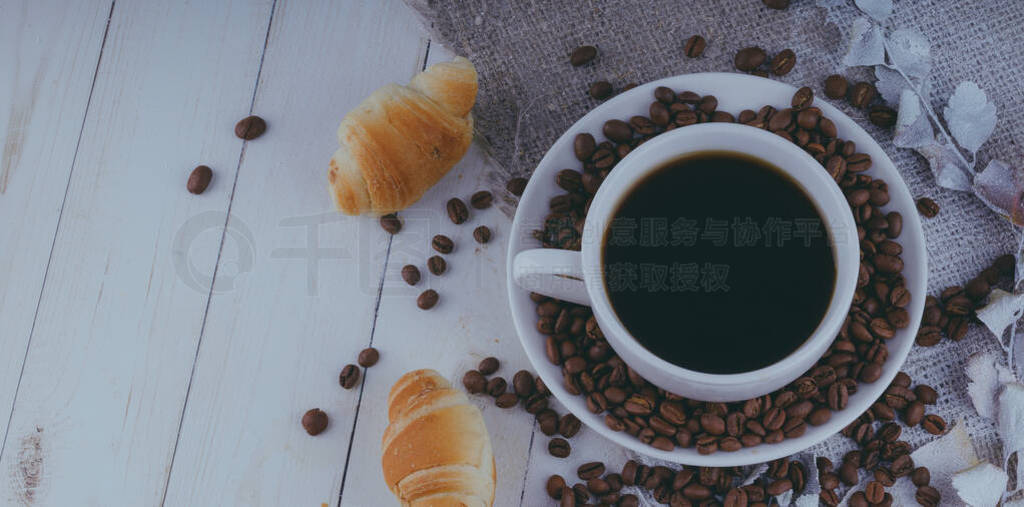 A steaming cup of coffee with coffee beans and a croissant on vi