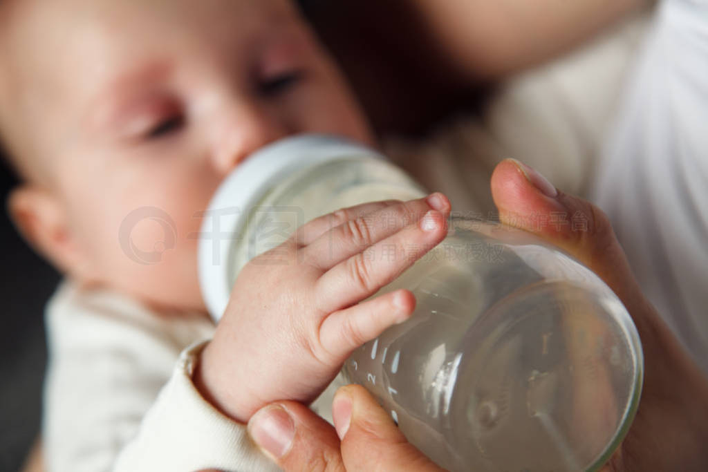 Baby drinking milk from glass bottle holding by father. Healthy