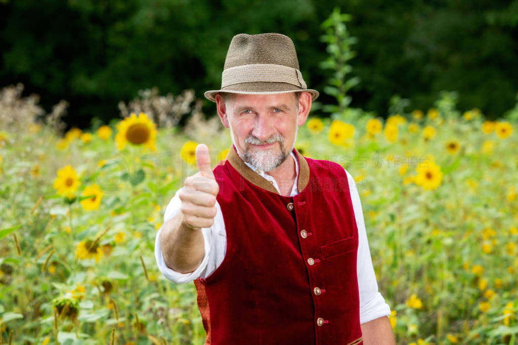 handsome bavarian man in his 50s standing in garden with thumbs