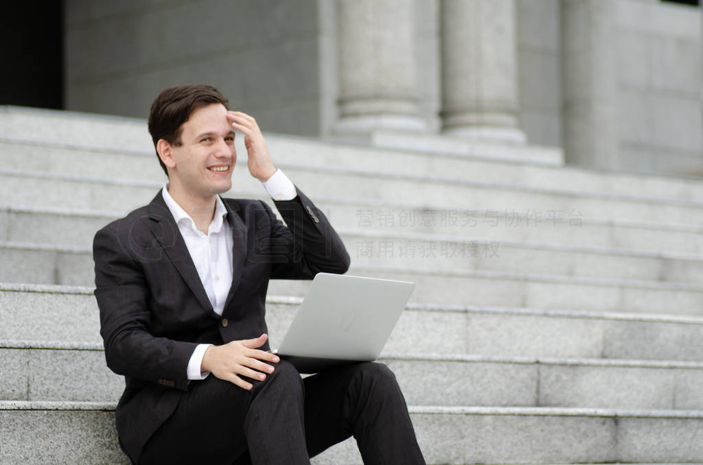 smiling young business man sitting on stairs and working with hi