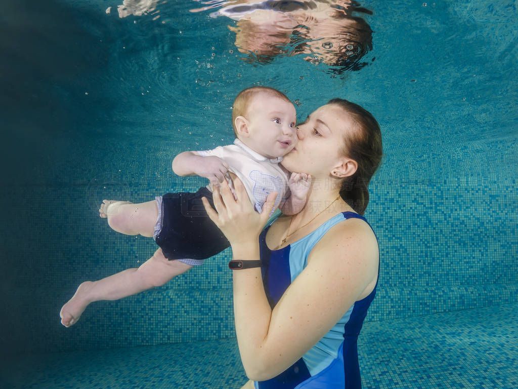 In blue pool young mother swimming with happy baby son dives und