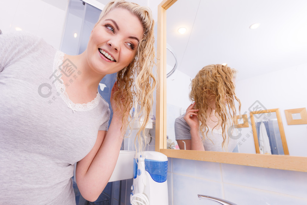 女子在浴室潮湿的长卷发看着镜子保重的白肤金发的女孩刷新她的发型在