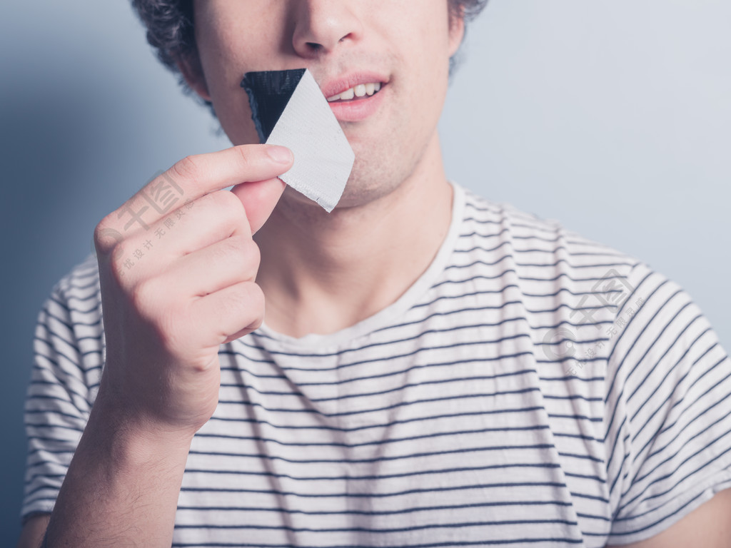 一名年轻男子正在撕掉一张捂住他的嘴的胶带