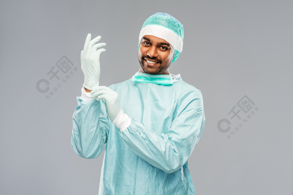 外科医生把手套放的防护服的在灰色背景印度男医生或外科医生戴上手套