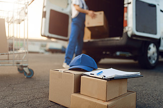 包裹箱子和蓋帽，背景的送貨員，送貨業務男子站在車輛，男性交付，快遞或運輸工作的紙板包裝