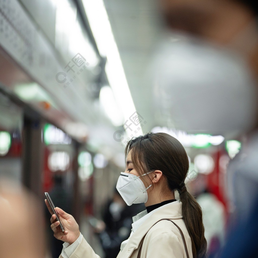 戴口罩的年轻女人在地铁里看手机