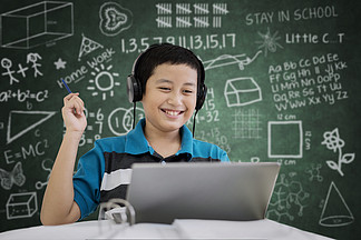 青春期學生用筆記本電腦學習時的圖片在黑板上涂鴉的教室里聽音樂