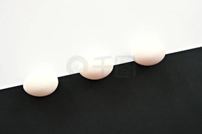 帶白杯的雞蛋位于半白半黑背景的前面 - 白色雞蛋的概念和強烈的對比作為背景與小陰影