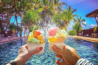 夫婦與美麗的明亮的甜意大利冰淇淋與不同的口味在手中。熱帶海灘全景的背景與椰子棕櫚樹。蘇梅島, 泰國