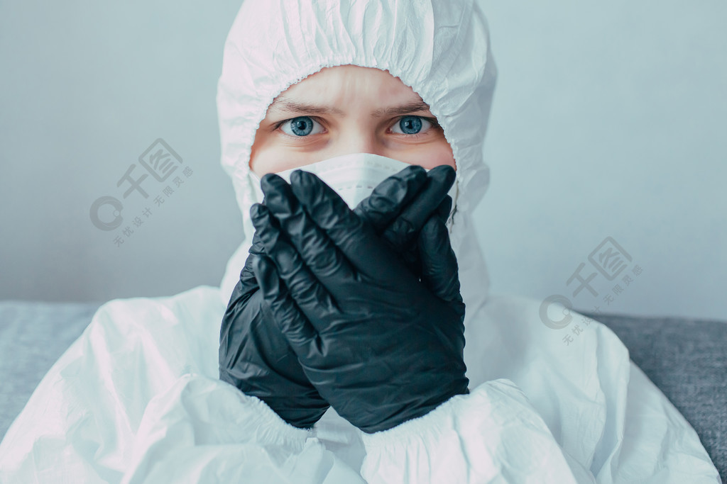 戴着医疗面罩身穿病毒性防护服的护士双手戴着黑色手套捂住脸焦虑地