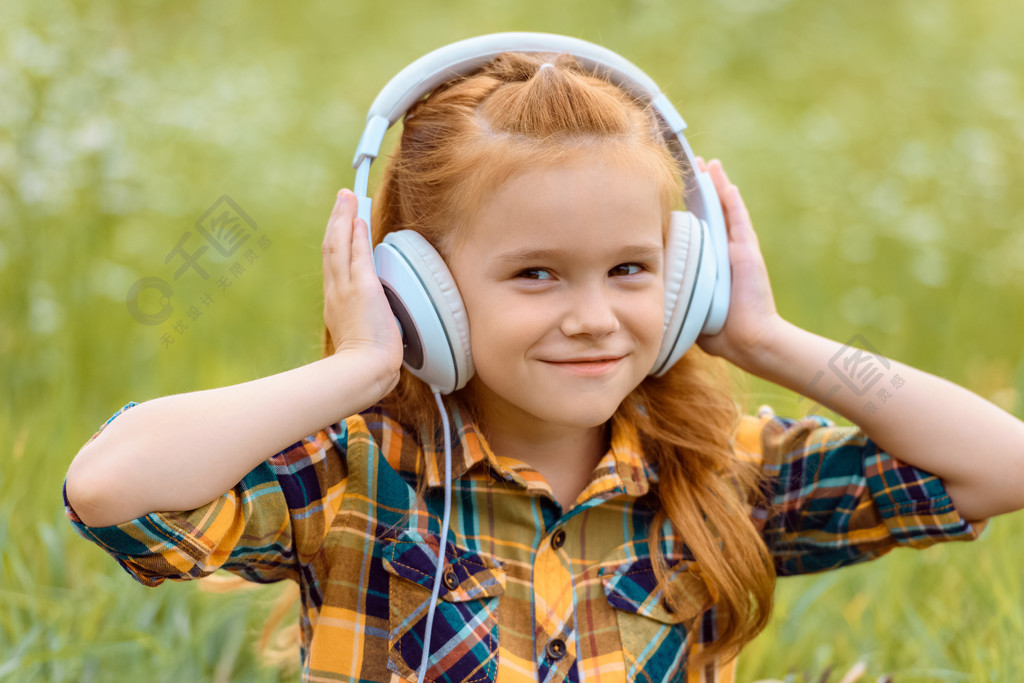 微笑的孩子的画像在背景绿色草的耳机听音乐