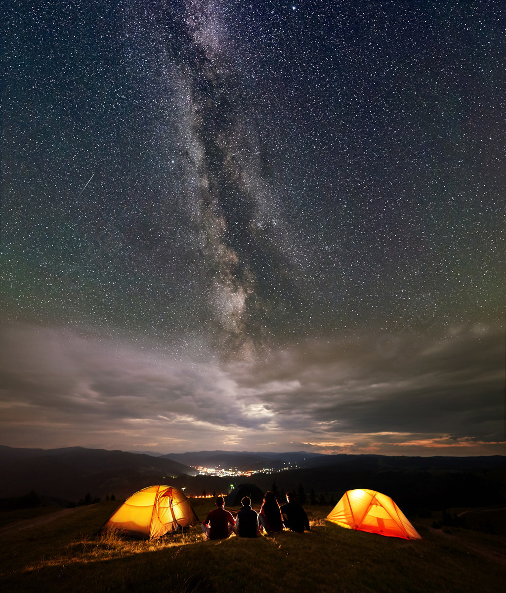 四名徒步旅行者坐在两个橙色帐篷营地, 晚上享受美丽的星空和银河.