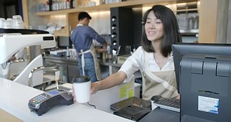 美丽的亚洲妇女做外卖咖啡的客户谁支付的非接<i>触</i>式移动电话信用卡系统