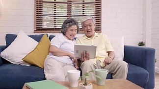 亚洲老年夫妇在家里的客厅里用平板电脑看电视