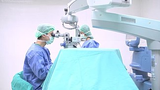 眼科外科医生在工作。年轻的白种男性外科医生与他的美丽的中国助理妇女执行手术的一个资深病人。真正的手术室室。医疗理念.