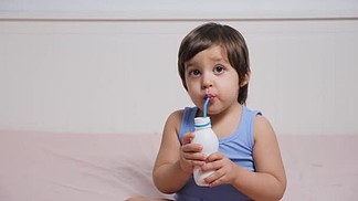 穿着蓝色 t恤的男婴坐在家里的<i>床</i>上喝牛奶