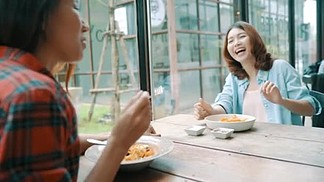 美丽快乐的亚洲女同性恋同志夫妇坐在一边吃着一盘意大利海鲜面条和法式薯条在餐馆或咖啡馆