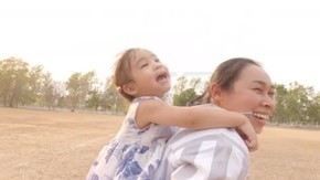 快乐的小女孩坐在妈妈的背上跑在公园里。幸福家庭和童年的概念.