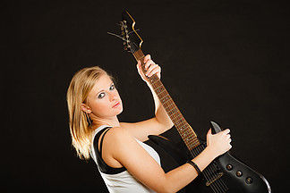 音乐，歌唱概念。在黑色背景上拿着电吉他的金发音乐才<i>华</i>横溢的女人。拿着电吉他的金发女人，黑色背景