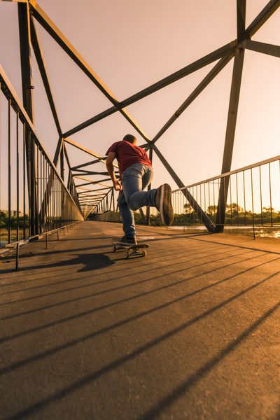 年轻的滑板手在日落时通过人行道桥加速