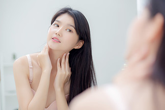 美丽性感的年轻亚洲女性照镜子在颈部和信息上涂抹奶油，美丽的女孩涂抹润肤露护肤以<i>保</i>持健康和柔软的水合作用，治疗和化妆品与<i>保</i><i>湿</i>剂。