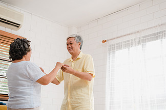亚洲老年夫妇在家里客厅听音乐时一起跳舞，<i>甜</i><i>蜜</i>的夫妇在家里放松时享受爱情时刻。生活方式高级家庭在家放松概念。