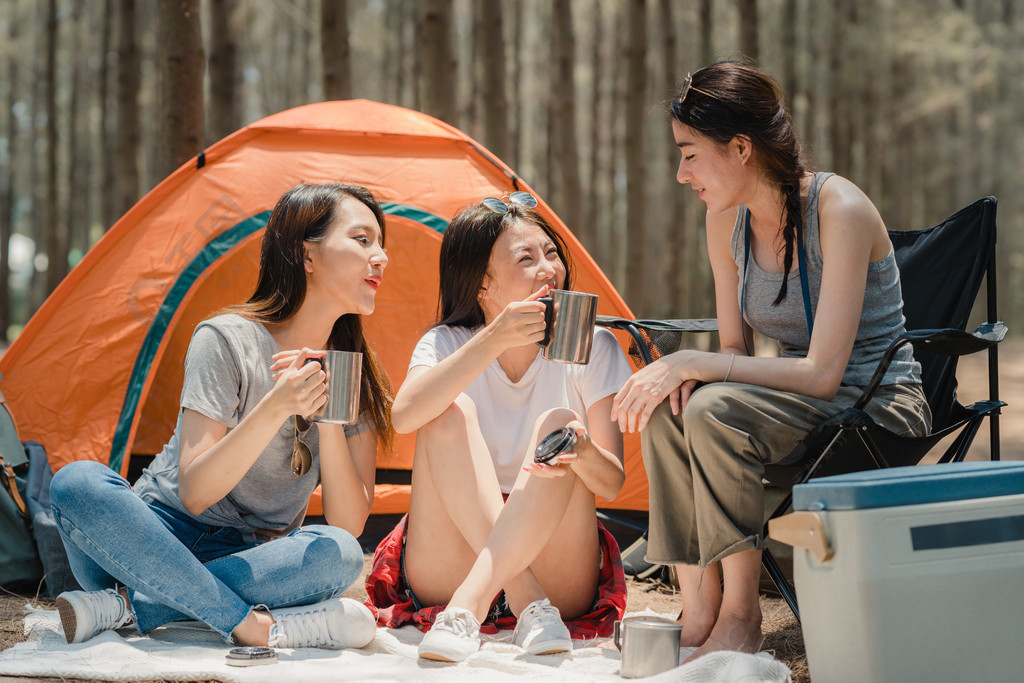 一群年轻的亚洲朋友在森林里露营或野餐，十几岁的女性在帐篷前享受谈话的时光。妇女在暑假期间进行冒险活动和旅行。