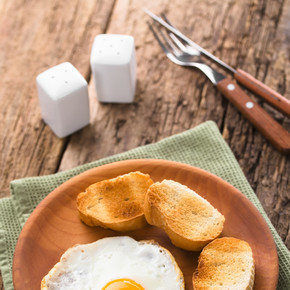 一个新鲜的煎蛋，一面朝上，一面是烤面包片，放在木盘、餐具、盐和胡椒瓶上（选择性聚焦，聚焦在蛋黄的前面）。烤面包煎蛋