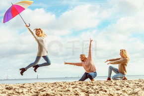 三个女人开心地打着五颜六色的伞跳来跳去。女性朋友在户外玩得开心。女性用雨伞跳跃