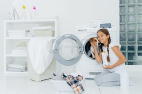 一张漂亮女孩在洗衣机里抚摸纯种狗的照片，拿着洗衣粉，去装洗衣机，忙着洗衣服和做家务，在家洗衣服，在室内摆姿势。