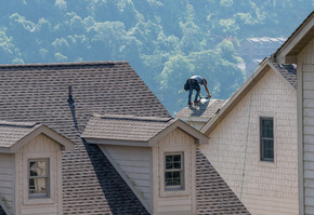 年轻的屋顶承包商在高出地面的联排别墅屋顶上更换旧瓦。年轻的屋顶承包商在高出地面的屋顶上钉木瓦