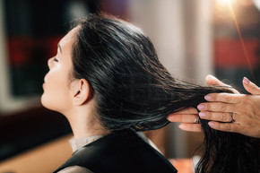 美发师在女人长长的黑发上涂抹活化油滴。发型师在女人的头发上涂抹活化油滴