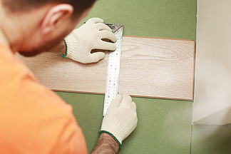 在房间里安装层压板或镶木地板，工人安装木复合地板，标记层压板的<i>长</i>度。在家里铺设复合地板。男人测量和标记.. 在房间里安装层压板或镶木地板，工人安装木复合地板，标记层压板的<i>长</i>度。在家里铺设复合地板。男人