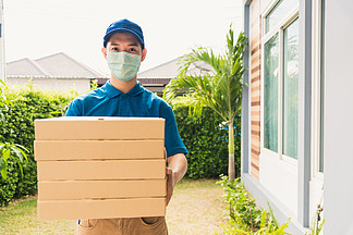 亚洲年轻<i>送</i>货员快递员在宵禁检疫流行性冠状病毒COVID-19下，在家门口<i>发</i><i>送</i>和拿着盒装快餐比萨饼，他的防护面罩服务客户