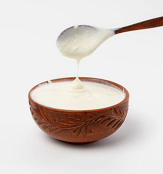 棕色陶瓷碗中的酸奶油，白色背景上的木勺，发酵乳制品