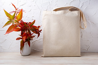 <i>帆</i><i>布</i>手提袋样机与白色花瓶中的红色秋草。用于品牌展示的质朴亚麻购物袋模型