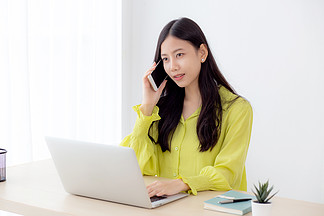 年轻的亚洲女商人在家庭办公室工作并打电<i>话</i>在家里取得成功，女商人在办公桌上使用笔记本电脑，女性在工作场所会<i>说</i><i>话</i>的智能手机，沟通概念。