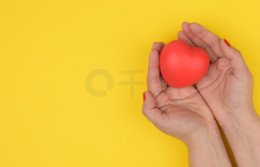 女性双手捧着红色的心，黄色的背景。爱与捐赠概念，复制空间