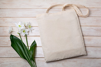 <i>帆</i><i>布</i>手提袋样机与木桌上的白百合。用于品牌展示的质朴亚麻购物袋模型