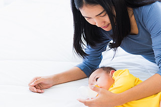 美丽的亚洲年轻母亲在白<i>床</i>上用奶瓶喂养婴儿新生儿的肖像，孩子从妈妈那里喝奶，保健和医疗