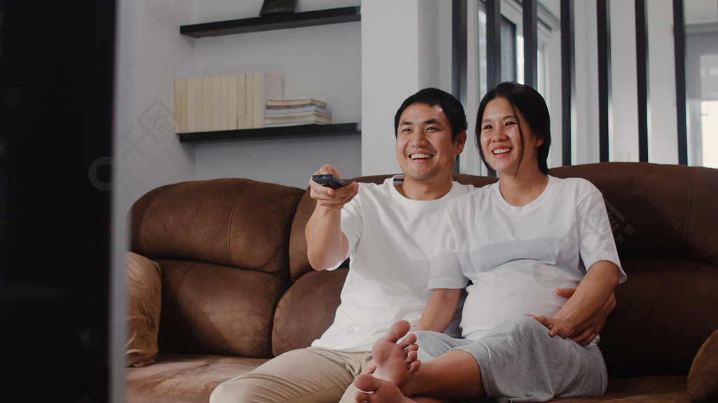 年轻的亚洲怀孕夫妇看电视妈妈和爸爸在照顾婴儿的同时感到幸福的微笑
