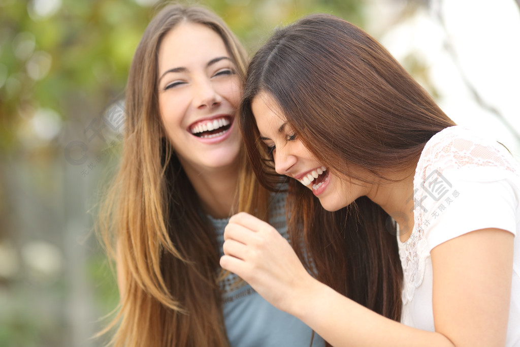 两个快乐的女朋友在绿色背景的公园里一起笑