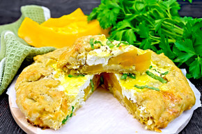 木板背景上的南瓜饼、咸羊乳酪、鸡蛋、奶油和香草、绿色餐巾、罗勒和欧芹